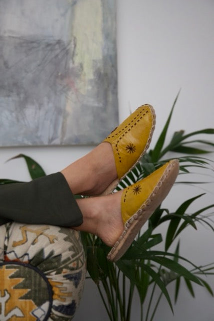 Leather handmade Egyptian slippers, mustard yellow leather on top and tan leather sole, white hand stitching through the yellow leather, pointed toe and flat sole